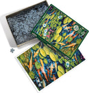 A Cobble Hill jigsaw puzzle titled 'Koi Pond' featuring vibrant artwork of koi fish swimming among lily pads and colorful flowers. The image shows the puzzle pieces in a box, alongside the completed picture on the table.