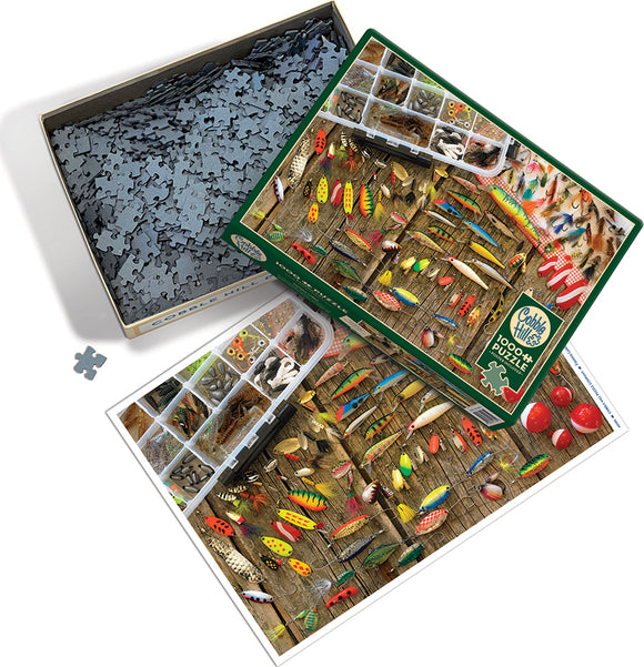 Cobble Hill Fishing Lures jigsaw puzzle featuring an assortment of colorful fishing lures displayed in a wooden compartment, with a complete puzzle image alongside. The box contains numerous interlocking pieces for a challenging and fun activity.