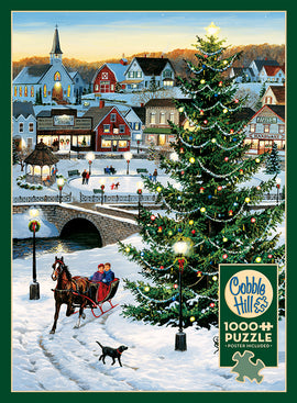 A jigsaw puzzle titled Village Tree by Cobble Hill featuring a picturesque winter village scene. In the foreground, a horse-drawn sleigh carries two children, while a black dog runs alongside. The vibrant Christmas tree is adorned with colorful lights, and the snowy landscape is dotted with cheerful townsfolk, shops, and a softly glowing lamppost. A tranquil bridge spans a frozen river, adding to the festive ambiance.