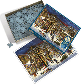 The product titled 'Tis the Season' by Cobble Hill is a jigsaw puzzle featuring a festive winter scene. The image shows an open box with numerous jigsaw pieces scattered around. The top lid displays a colorful illustration of a lively holiday street scene with people enjoying various winter activities, snow-covered buildings, and trees adorned with lights. The scene captures a cozy, charming atmosphere of the holiday season, perfect for family gatherings and seasonal fun.