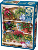 Flower Cupboard jigsaw puzzle by Cobble Hill featuring a vibrant illustration of a wooden shelf adorned with various potted flowers, baskets, and gardening tools. The design includes details such as colorful flower pots, lush greenery, and charming decorative elements, perfect for flower enthusiasts and puzzle lovers alike.
