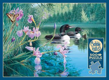 Iris Cove Loons jigsaw puzzle by Cobble Hill featuring a serene lakeside scene with two loons swimming in crystal-clear water surrounded by vibrant flowers and a butterfly. The artwork captures the tranquility of nature, making this a perfect 500-piece puzzle for nature lovers and puzzle enthusiasts alike.