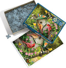 A colorful jigsaw puzzle titled 'Summer Birdhouse' by Cobble Hill. The box is open, revealing an array of puzzle pieces alongside the image of a birdhouse surrounded by vibrant flowers and various birds, including cardinals and bluebirds, creating a lively garden scene.