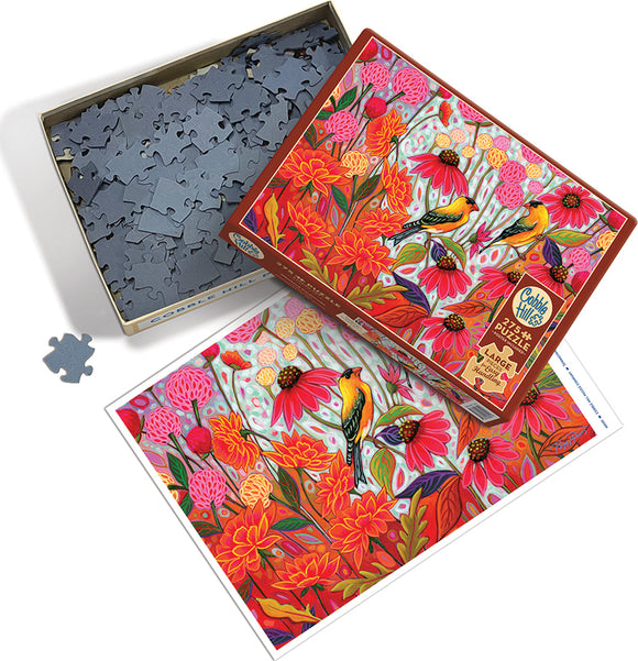 A colorful jigsaw puzzle titled 'Springtime Goldfinches' by Cobble Hill. The image showcases bright illustrations of goldfinches perched amidst vibrant flowers and foliage. The puzzle pieces are spread out in an open box, with a reference image of the completed puzzle alongside, capturing the rich colors and intricate details of the design.
