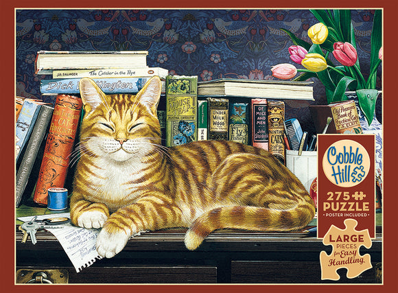 A jigsaw puzzle featuring a serene orange tabby cat lounging on a wooden desk surrounded by colorful books and a vase of tulips. The cat has a content expression, with its eyes half-closed, and is positioned in front of various titles related to cats and fishing, alongside a blue cup and a notepad. The intricate background displays floral patterns.