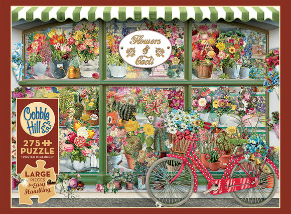 A vibrant jigsaw puzzle featuring a charming flower and cactus shop front. The scene displays an array of colorful flowers in pots, hanging plants, and various cacti, all framed by a green-striped awning. A red bicycle with a basket filled with flowers is positioned in front of the shop, enhancing the picturesque setting. The puzzle includes 275 large pieces for easy handling and comes with a poster.