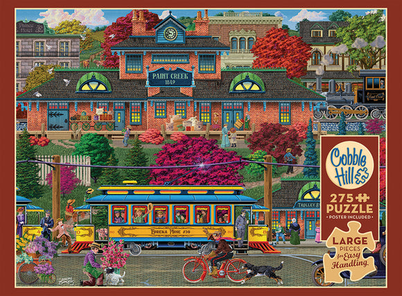 A colorful jigsaw puzzle titled 'Trolley Station' by Cobble Hill, featuring a vibrant street scene with a vintage trolley, a brick building labeled 'Paint Creek 1849', lush greenery, and people engaged in various activities. The puzzle includes 275 large pieces designed for easy handling, and a poster is included for reference.