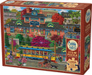 Cobble Hill Trolley Station jigsaw puzzle featuring a vibrant, detailed illustration of a historic trolley station scene with people interacting, colorful trees, flowers, and vintage vehicles. The box includes a 275-piece puzzle and a poster for reference.