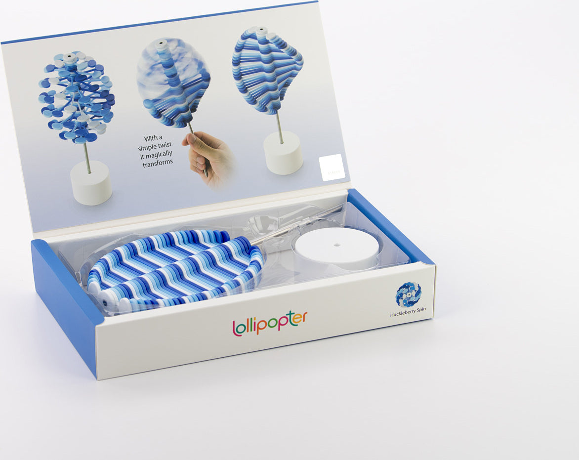 The Lollipopter Huckleberry Spin by Beyond 123 is a colorful and engaging fidget toy. The box showcases the toy, which features vibrant blue and white swirling patterns. The display indicates that it magically transforms with a simple twist, highlighting its playful design. The components are neatly arranged inside the box, suggesting creativity and fun for all ages.