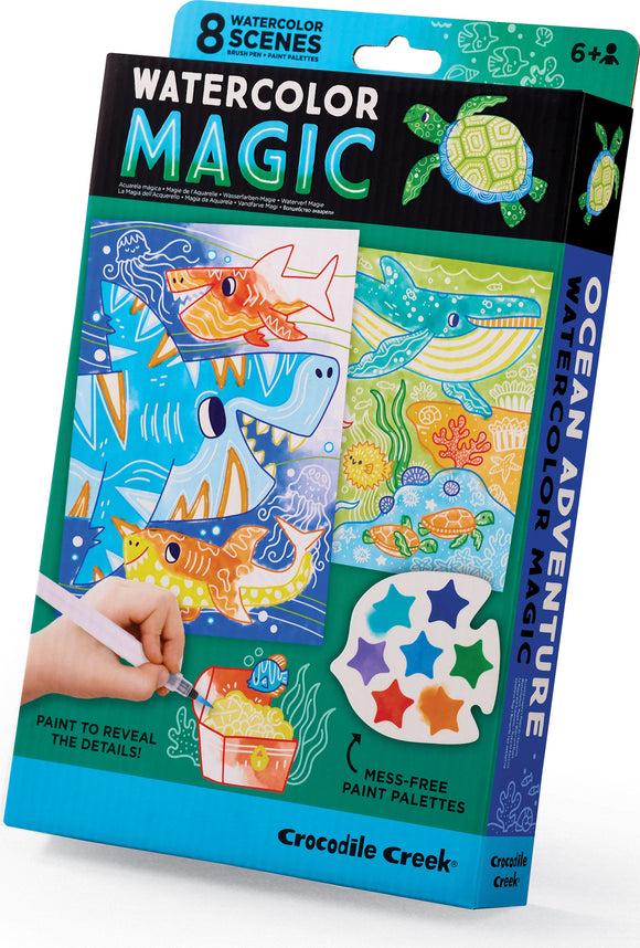 The Watercolor Magic Ocean Adventure kit by Crocodile Creek features eight watercolor scenes, each illustrating vibrant ocean life with images of sharks, turtles, and colorful fish. The kit includes a brush pen and mess-free paint palettes, designed for ages 6 and up. A hand holds the brush pen over a scene, demonstrating the painting process to reveal hidden details.