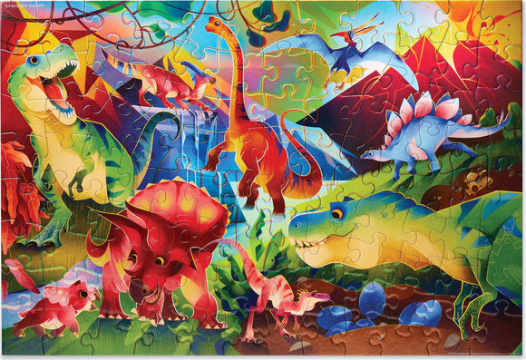 A vibrant jigsaw puzzle featuring a colorful dinosaur scene. Various dinosaurs, including a T-Rex, Triceratops, and Stegosaurus, are depicted in a prehistoric landscape with mountains and foliage. The puzzle showcases fun, whimsical artwork with bright colors and holographic foil details.