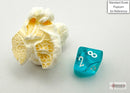 Chessex Trans Mini Teal and White 7 Polyhedral die displayed beside popcorn for scale. The die features clear teal coloring with white numbers, designed for tabletop games.