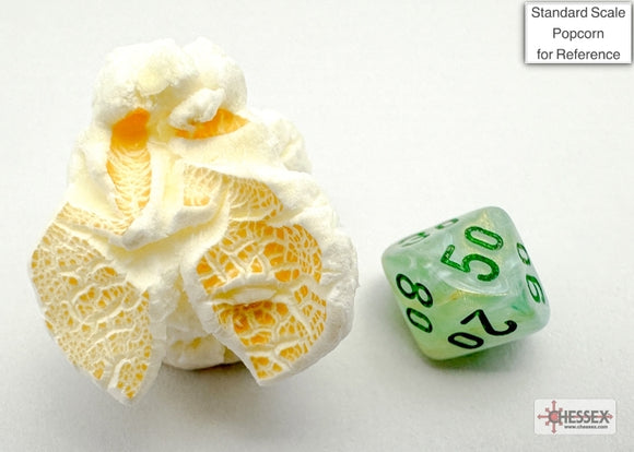 A close-up image showing a detailed, translucent green and dark green polyhedral die beside a piece of popcorn for scale. The die has numbers printed in a contrasting color, enhancing visibility. The background is plain to focus on the items.