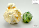 A green and dark green marbled D20 dice from Chessex, displayed next to a piece of popcorn for size reference. The dice features clear numbers and a glossy finish, highlighting its vibrant colors perfect for tabletop games.