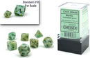 A clear display box containing a mini polyhedral 7-die set in marble green and dark green colors. The dice are numbered with black ink and include a standard d10 die for scale. Perfect for tabletop role-playing games.