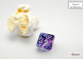 Nebula mini poly nocturn blu dice by Chessex, featuring a mesmerizing purple and blue swirl design with white numbers. A piece of popcorn is included for size reference, enhancing the visual context of the game accessory.