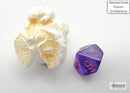 A Mini Borealis RPG dice by Chessex in purple and gold colors. The seven-sided die is placed next to a piece of popcorn for scale, showcasing its intricate design and vibrant color.