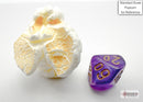 Chessex Mini Borealis Purple/Gold 7-sided die displayed next to a piece of popcorn for scale. The die features a vibrant purple color with gold numbering, ideal for tabletop gaming.