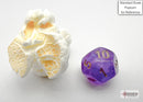 A purple and gold ten-sided die from Chessex, displayed next to a piece of popcorn for scale. The die features numbers in a clear, readable font and showcases a vibrant, shimmering finish. Perfect for tabletop games and RPGs.