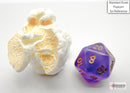 Mini Borealis purple and gold 7-sided die from Chessex, showcased alongside a piece of popcorn for size reference. The die features a smooth, translucent finish with vibrant gold numbers.