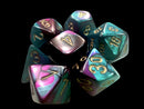 A set of Mini Gemini RPG dice featuring a vibrant purple-teal color scheme with gold numbering. The dice are arranged in a clustered pile, showcasing various shapes including d20s, d12s, and d6s, ideal for tabletop gaming.