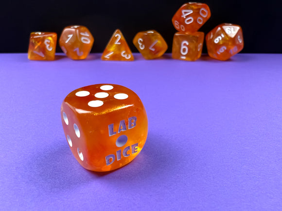 A vibrant Borealis Blood Orange and White Luminary 7 Piece Dice Set by Chessex. The set features a variety of polyhedral dice with a glossy orange finish and white numbers. The largest die displays 'LAB DICE' engraved, standing out against a purple surface, with additional dice featuring numbers arranged artistically in the background.