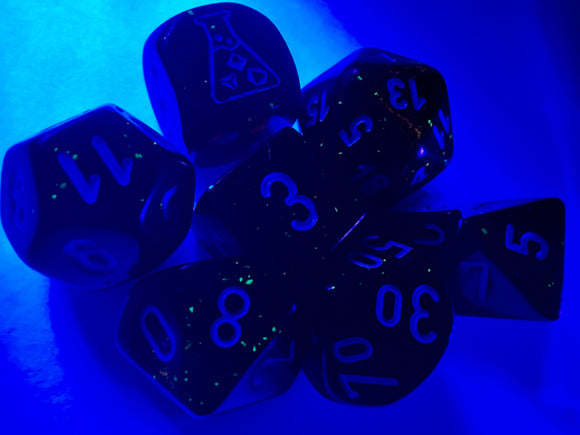 A vibrant 7-piece Luminary dice set in Borealis Blood Orange and White, featuring clear numerical markings. The dice are artistically showcased under blue lighting, highlighting their unique luminosity and intricate design, perfect for tabletop gaming enthusiasts.