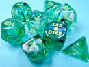 A colorful 7-piece dice set named 'LAB DICE: Borealis Kelp/Light Green Luminary' made by Chessex. The dice feature translucent green bodies with luminous yellow numbers, showing various standard polyhedral shapes including d20, d12, d10, d8, d6, and d4. The set is laid out on a light blue backdrop, highlighting its vibrant colors.