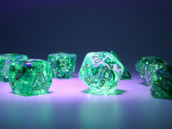A vibrant 7 piece dice set by Chessex, featuring Borealis Kelp and light green luminary color. The dice are translucent with intricate designs, including numbers and a laboratory flask symbol. Illuminated under purple light, the set showcases a whimsical glow, perfect for tabletop gaming enthusiasts.