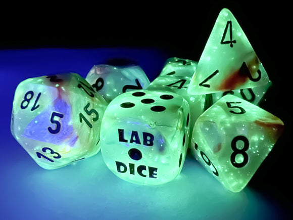 A vibrant 7-piece dice set from Chessex featuring lustrous sea shell and black luminary colors. The set includes a variety of polyhedral dice, glowing under a blue light, with numbers clearly marked in black against an iridescent background. The centerpiece die showcases 'LAB DICE' prominently, adding a unique touch to this gaming accessory.