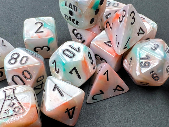 A vibrant 7-piece polyhedral dice set by Chessex, featuring lustrous sea shell and black luminary colors. The dice include various shapes, such as d4, d6, d8, d10, d12, and d20, all with bold black numerals. The set is artistically arranged, showcasing the iridescent finish and unique patterns of each die, perfect for tabletop games and RPG enthusiasts.
