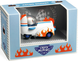 The Crazy Motors: Astro Rocket, a whimsical collectible toy featuring a white rocket-shaped vehicle with orange flames and blue wheels, displayed in a colorful box. The packaging has a checkered design and the brand logo prominently featured on the front.