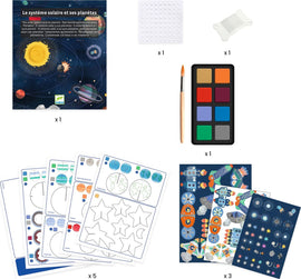 A Solar System Decorative Mobile DIY kit by DJECO featuring a colorful box with planets and the sun illustrated. The kit includes 5 sheets with designs for planets and stars, a watercolor paint set, a brush, and adhesive dots for assembly.