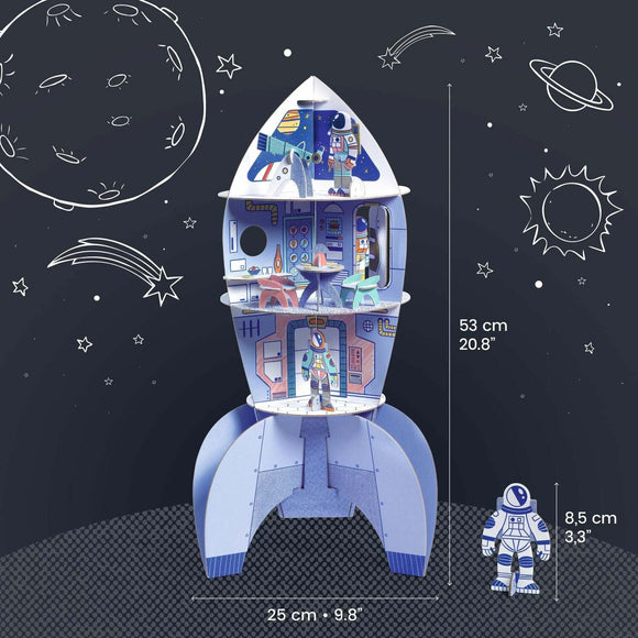 A colorful DIY kit of a space rocket featuring multiple levels and an astronaut figurine. The rocket includes illustrated interiors with tables and chairs, designed to inspire imaginative play and creativity. Dimensions shown are 53 cm tall and 25 cm wide.