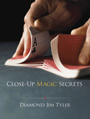 A close-up view of hands expertly fanning a deck of playing cards, displaying the ace of clubs. The book titled 'Close-Up Magic Secrets' by Diamond Jim Tyler is prominently featured, aimed at teaching readers various magic tricks and techniques using card sleight of hand.