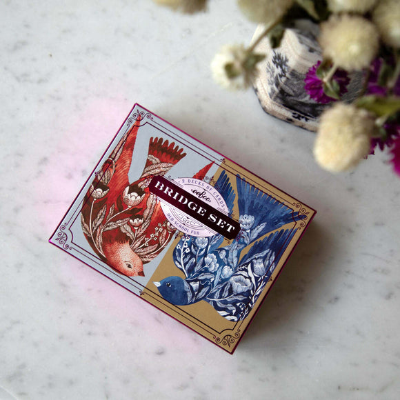Eeboo's Bridge Playing Cards featuring Malin's Birds. The beautifully illustrated box showcases two decks of cards, one with red and the other with blue bird designs surrounded by floral accents. Ideal for classic card games.