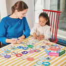 A mother and daughter engage in play with the Simple Words Hexagon Puzzle by Eeboo, featuring colorful hexagonal puzzle pieces with words and images. The scene shows the daughter focused on placing a piece as the mother holds additional pieces, with a bright and cheerful atmosphere in a cozy room.