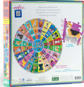 An enchanting 500-piece round jigsaw puzzle titled 'Dogs of the World' by Eeboo. The design features a colorful collage of dog breeds from around the globe, with a vibrant border and an image of a puzzle piece showing a Corgi. The box displays playful dog illustrations and the puzzle's dimensions, 23 inches in diameter.