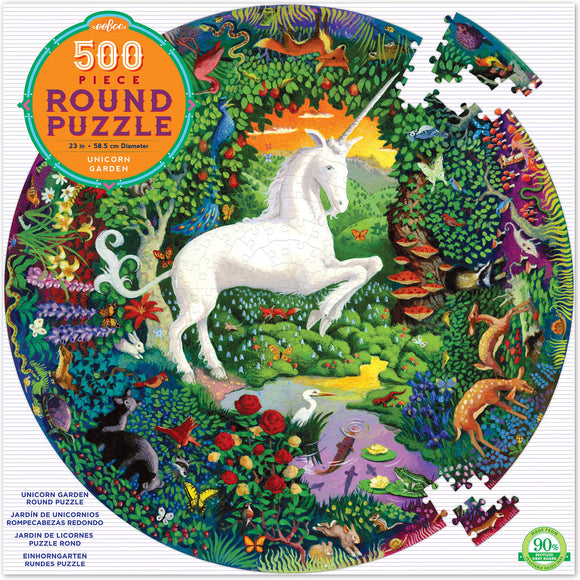 A colorful 500-piece round jigsaw puzzle titled 'Unicorn Garden' by Eeboo. The design features a majestic white unicorn amidst a lush landscape filled with vibrant flowers, butterflies, and various animals in a magical garden setting.