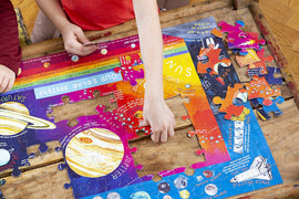 A colorful jigsaw puzzle titled 'Our Solar System' made by Eeboo is being assembled on a wooden table. Children’s hands are placing pieces, showcasing planets and educational details about the solar system.