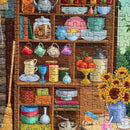 A vibrant 1000-piece jigsaw puzzle featuring a cozy kitchen scene filled with colorful cups, jars, and a sunflower arrangement atop a wooden shelf. Items like fruits, dishes, and cookbooks are displayed, inviting a sense of warmth and nostalgia.