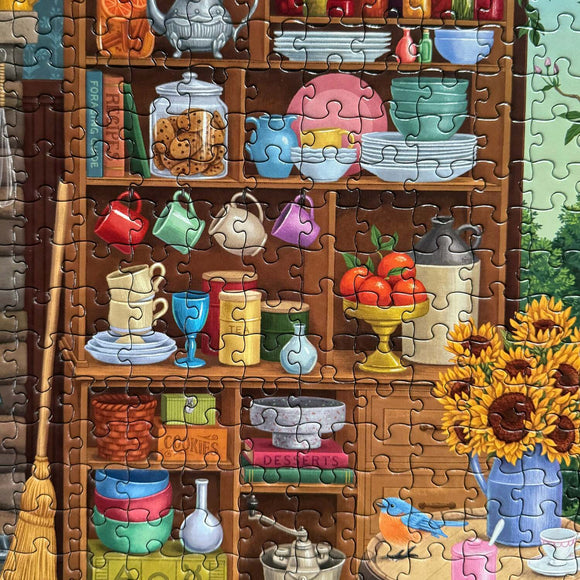 A vibrant 1000-piece jigsaw puzzle featuring a cozy kitchen scene filled with colorful cups, jars, and a sunflower arrangement atop a wooden shelf. Items like fruits, dishes, and cookbooks are displayed, inviting a sense of warmth and nostalgia.
