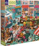 The English Green Market jigsaw puzzle by Eeboo features a vibrant scene of a bustling outdoor market filled with colorful fruits, vegetables, and flowers. The puzzle box showcases charming shops like a bakery and a bookstore, surrounded by shoppers and vendors. The artwork is whimsical and detailed, inviting users to immerse themselves in the market's lively atmosphere.