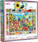 The Seagull Garden jigsaw puzzle by Eeboo is a vibrant 1000-piece puzzle featuring a colorful illustration of a seaside garden filled with flowers, birds, and marine life. The box displays the finished image, showcasing sunflowers, starfish, and sailboats against a blue sky and ocean backdrop. The actual piece size is highlighted, emphasizing its quality and detail.
