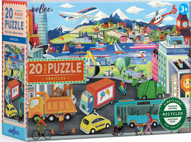 Eeboo 20 Piece Jigsaw Puzzle featuring a vibrant, illustrated scene of various vehicles in action, including trucks, boats, and helicopters, set against a colorful backdrop of buildings, mountains, and trees. The puzzle is designed for children ages 3 and up, promoting cognitive development and creativity.