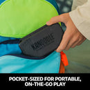 A person is placing the Kanoodle Ultimate Champion mechanical puzzle into a pocket of a colorful backpack. The puzzle is compact and designed for easy portability, making it perfect for on-the-go play. The backpack features vibrant colors.