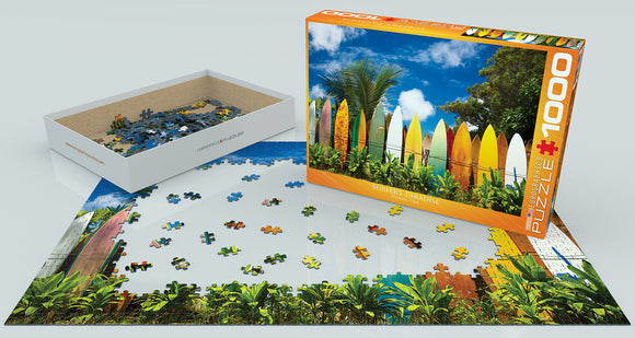 Surfer's Paradise Hawaii jigsaw puzzle by Eurographics, featuring a vibrant image of colorful surfboards against a lush tropical backdrop. The puzzle box stands next to its partially completed image, showcasing scattered pieces in a white tray. Perfect for puzzle enthusiasts and beach lovers alike.