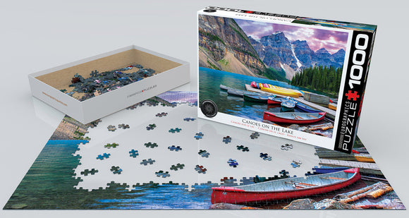 A Eurographics jigsaw puzzle titled 'Canoes on the Lake'. The image shows an array of colorful canoes on a serene lake surrounded by mountains. The puzzle is partially assembled, with scattered pieces still in the tray and on the table. The box displays a vibrant, picturesque scene capturing the beauty of the outdoors.