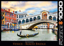 Eurographics jigsaw puzzle featuring the iconic Rialto Bridge in Venice. The art depicts a scenic view with colorful buildings along the Grand Canal, a gondolier navigating the waters, and a beautiful sky at sunset. Ideal for puzzle enthusiasts and lovers of Venice's architectural beauty.