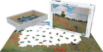The Poppy Field jigsaw puzzle by Claude Monet, produced by Eurographics. The box features the iconic painting with a scenic field of red poppies and a blue sky. The surrounding area shows colorful puzzle pieces scattered on the table, ready to be assembled.